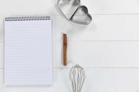 Top view of a composition with an empty page in notebook with cookie cutters and whisker, arranged on on a white textured wooden surfaceの写真素材