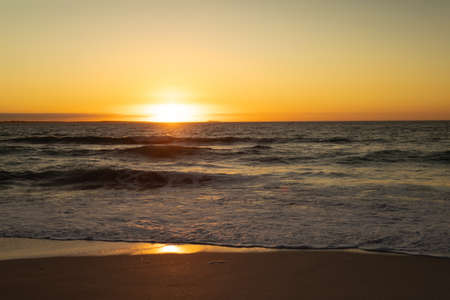 Beautiful view of the sun setting over the ocean waves and fine sand on the horizon.の写真素材