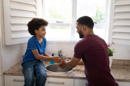 Mixed race father with son enjoying family time together at home, social distancing and self...