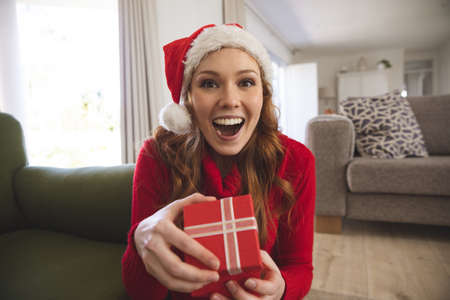 Portrait of Caucasian woman spending time at home, in living room, smiling, wearing Christmas hat,...