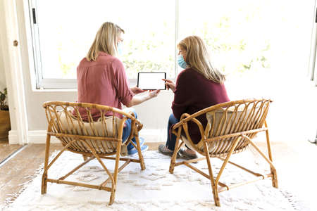 Senior Caucasian woman spending time at home with her adult daughter,
sitting on couch talking and...