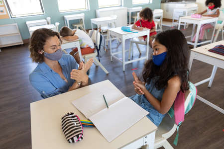 Caucasian female teacher wearing face mask at school, teaching children at school classroom. Education back to school health safety during Covid19 Coronavirus pandemic.の写真素材