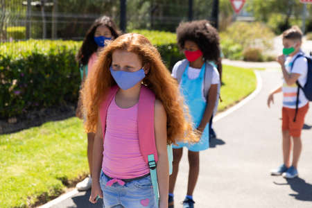 Multi ethnic group of school children wearing face masks, walking on the street. Education back to...