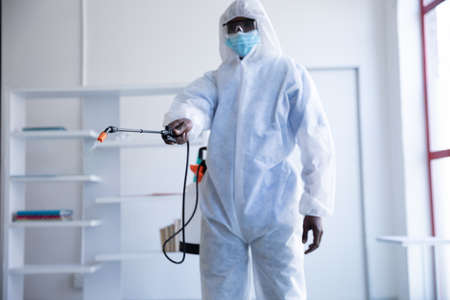 African american male doctor scientist wearing protective clothing and face mask, cleaning, spraying...