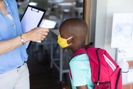 Multi ethnic group of school children wearing face masks, standing in line, having their temperature checked by a teacher. Education back to school health safety during Covid19 Coronavirus pandemic.の写真素材