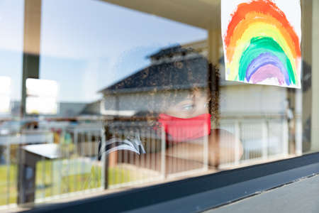 Schoolgirl wearing face mask, looking through a window. Education back to school health safety...
