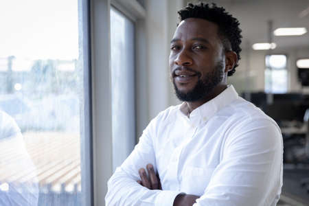 Portrait of African American businessman working in a modern office, standing by the window looking...