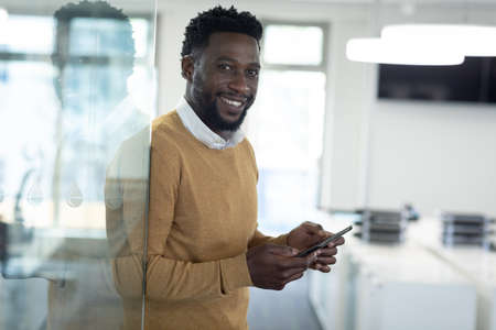 Portrait of African American businessman working in modern office, using smartphone and smiling to...
