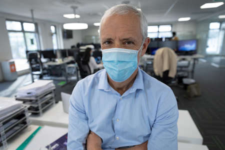 Portrait of senior Caucasian businessman wearing face mask working in a modern office, standing with...