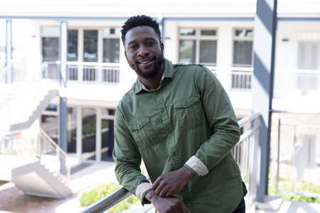 Portrait of confident African American businessman in a modern workplace standing on a balcony in...