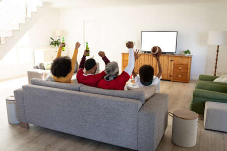 Multi generation African American family at home sitting on sofa in living room, watching sports on...