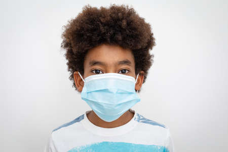 Portrait of African American boy with afro hair at home, wearing a mask and looking to camera....