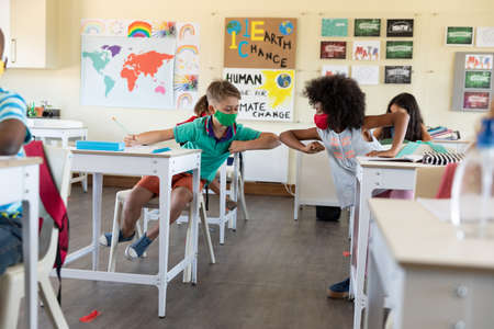 Caucasian female teacher wearing face mask at school, teaching children at school classroom....