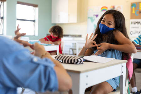 Caucasian female teacher wearing face mask at school, teaching children at school classroom. Education back to school health safety during Covid19 Coronavirus pandemic.の写真素材