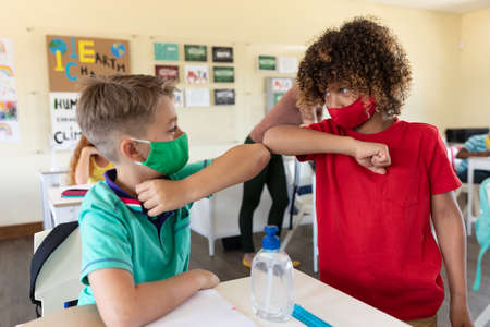 Caucasian female teacher wearing face mask at school, teaching children at school classroom....