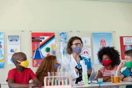 Caucasian female teacher wearing face mask at school, teaching children at school classroom....