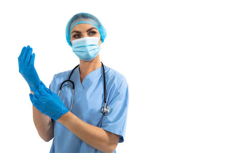 Portrait of Caucasian female surgeon putting protective surgical gloves, wearing scrubs, face mask...