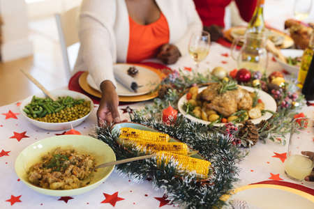 Mid section of woman picking up a food plate while sitting and having lunch on dining table in the living room at home. christmas festivity tradition celebration conceptの写真素材