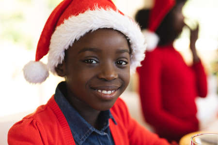 Portrait of boy wearing santa hat smiling having lunch on dining table in the living room at home.の写真素材