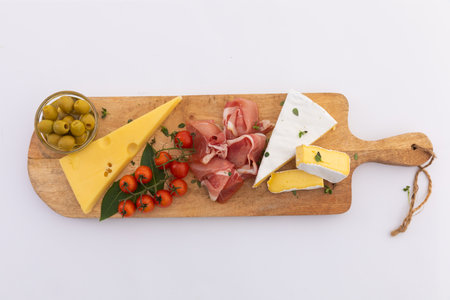 Olives, cheese, ham and cherry tomatoes on wooden board on white background. fresh produce...