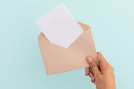 Hand of caucasian woman holding opened envelope with letter over pale blue background. greetings...