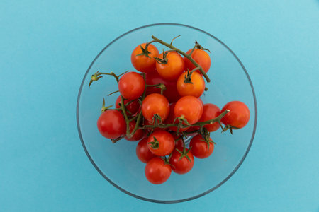 High angle view of bowl of fresh cherry tomatoes on blue background. fresh healthy vegetables copy space concept.の写真素材