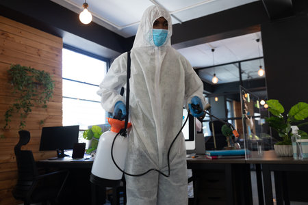 Mixed race cleaner wearing protective suit in an office. disinfecting the office. hygiene in workplace during coronavirus covid 19 pandemic.の写真素材