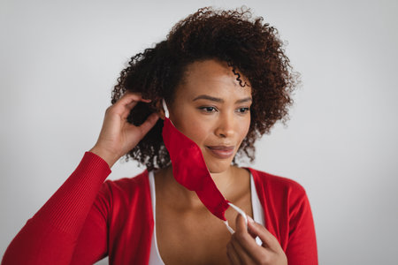 Portrait of african american woman removing face mask against grey background. hygiene and...