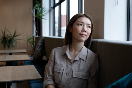 Asian woman looking out of window in creative office cafeteria. social distancing in business office...