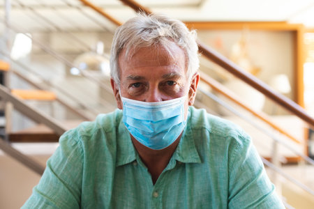 Portrait of senior caucasian man at home wearing face mask. self isolation during coronavirus covid 19 pandemic.の写真素材