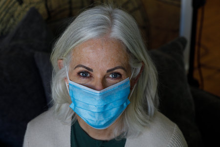 Portrait of senior caucasian woman wearing face mask at home. social distancing quarantine lockdown during coronavirus pandemicの写真素材