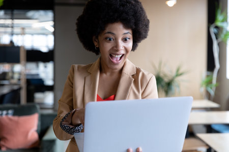 Smiling mixed race businesswoman using laptop during video call in office. technology and social distancing in business office workplace during covid 19 coronavirus pandemic.の写真素材
