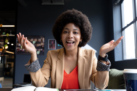 Mixed race businesswoman during video call in creative office, talking. technology and social distancing in business office workplace during covid 19 coronavirus pandemic.の写真素材