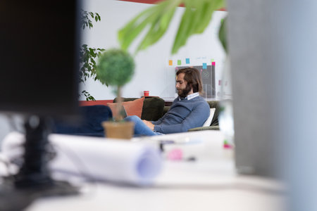 Caucasian businessman using laptop sitting on sofa in creative office. technology and social distancing in business office workplace during covid 19 coronavirus pandemic.の写真素材