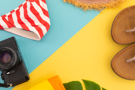 Sun lotion, flip flops, sunhat, bikini and camera on yellow and blue. summer holiday fun travelling...