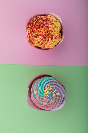 High angle view of two colourful cupcakes with sprinkles on purple and green background. food dessert fun copy space concept.の写真素材