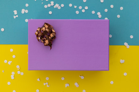 Purple gift box with ribbon and white confetti on yellow and blue background. happy birthday party...
