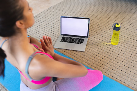 Mixed race woman practising yoga at home using her laptop. self isolation during covid 19 coronavirus pandemic.の写真素材