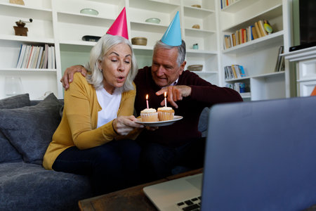 Senior caucasian couple celebrating birthday while having a video chat on laptop at home. social distancing quarantine lockdown during coronavirus pandemicの写真素材