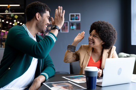 Happy diverse businessman and businesswoman high fiving in creative office. success teamwork in business office workplace during covid 19 coronavirus pandemic.の写真素材