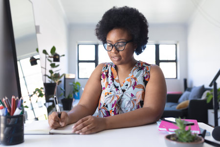 African american female vlogger recording a video writing in notebook. self isolation technology communication at home during coronavirus covid 19 pandemic.の写真素材