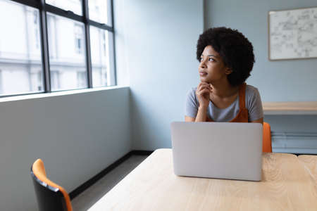 Mixed race businesswoman working in creative office. woman sitting at table and using laptop. social...