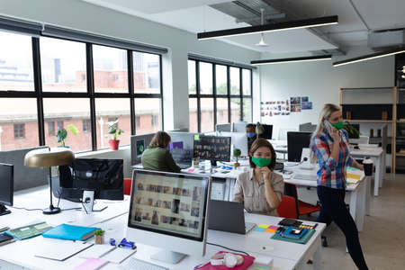 Diverse group of business people wearing face masks in creative office. group of people sitting at...
