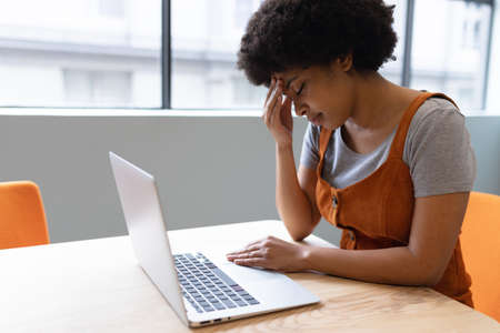 Mixed race businesswoman working in creative office. woman sitting at table and using laptop. social...