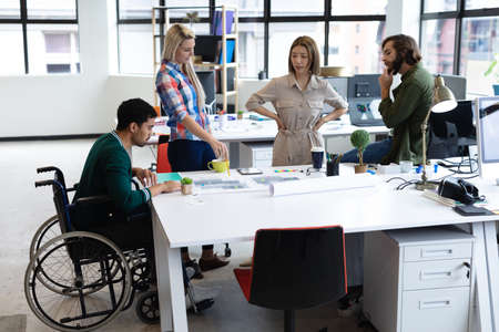 Diverse group of business colleagues looking at blueprints and discussing at table. equal...