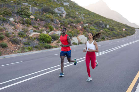 Fit african american couple in sportswear running on a coastal road. healthy lifestyle, exercising in nature.の写真素材