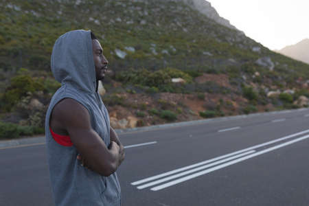 Fit african american man in sportswear standing on a coastal road. healthy lifestyle, exercising in...