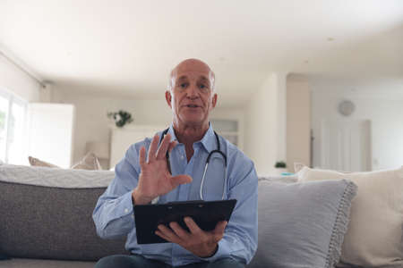 Senior caucasian male doctor having a video call using a digital tablet at home. medical...