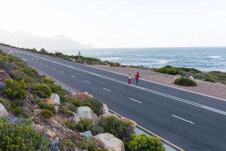 Fit african american couple in sportswear running on a coastal road. healthy lifestyle, exercising...