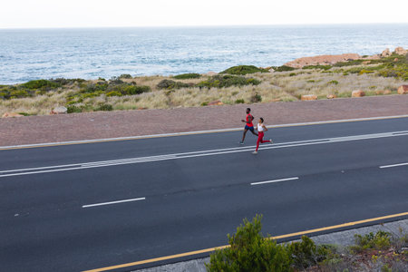 Fit african american couple in sportswear running on a coastal road. healthy lifestyle, exercising...